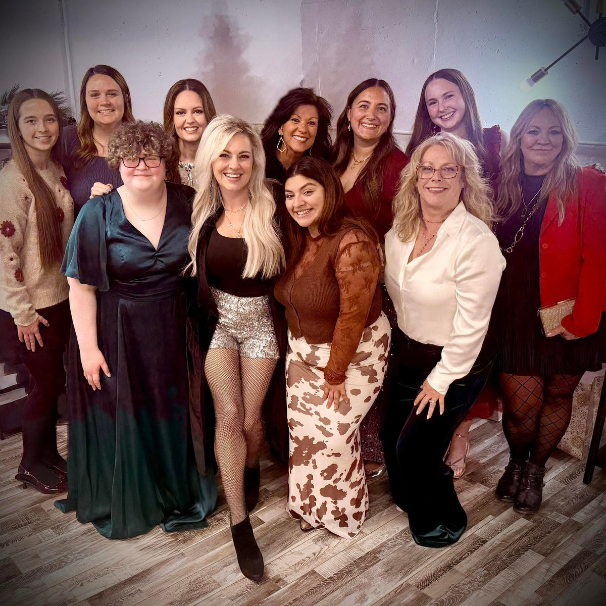 A group of ten women posing together in an indoor setting with a wood floor and a textured wall background.